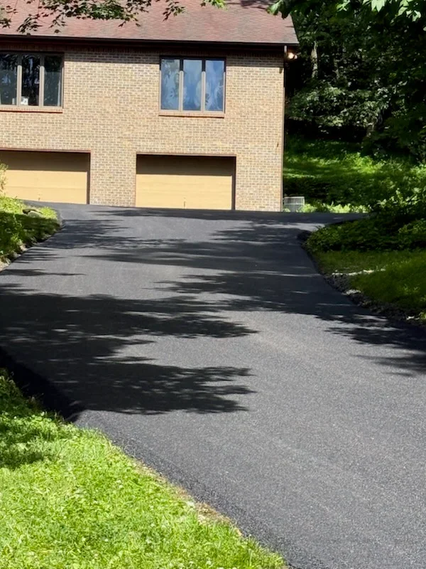 Newly paved black asphalt driveway in front of brick home with two-car garage