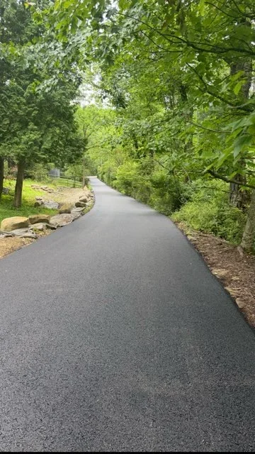 Newly paved asphalt driveway curving through wooded property with stone borders