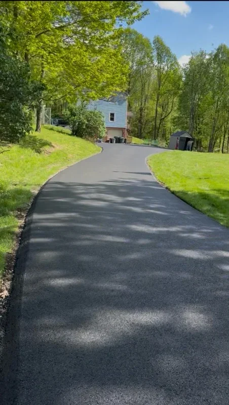 New asphalt driveway curving through green lawn with trees and house in background