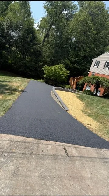 Newly paved black asphalt driveway with curved design and landscaped edges