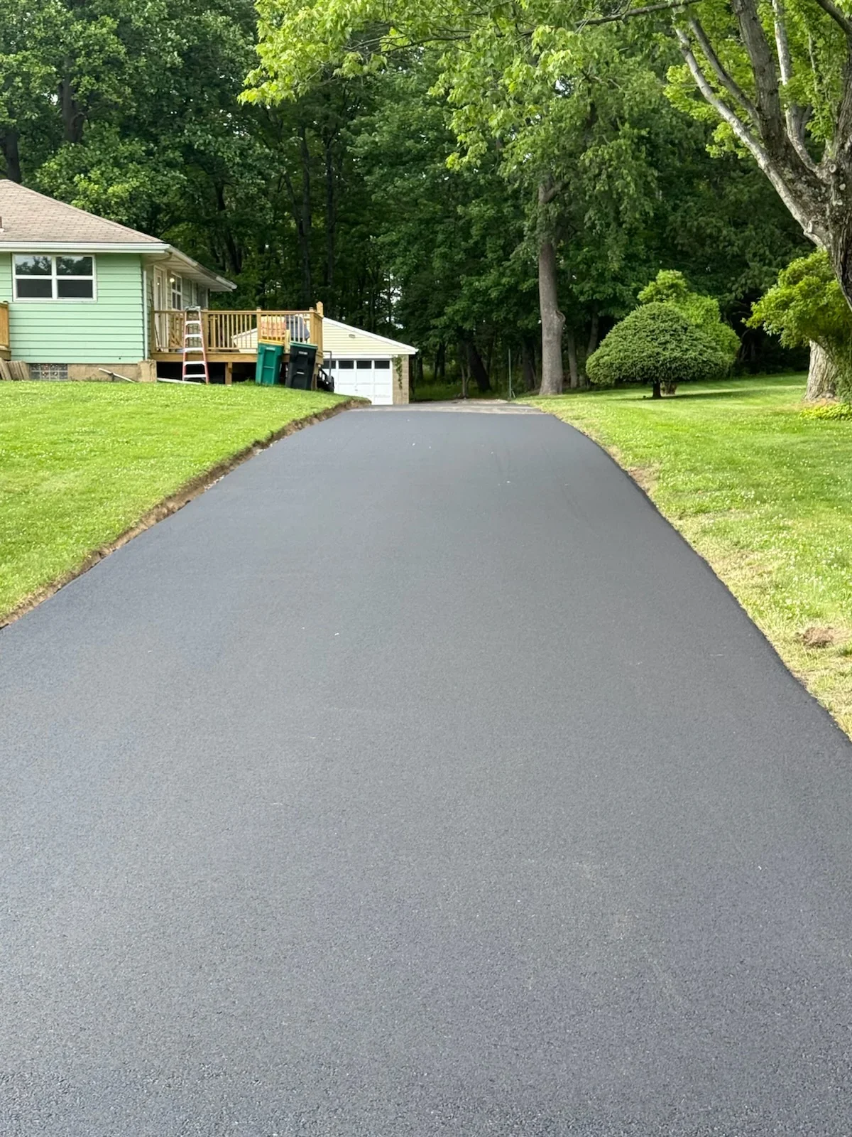 New black asphalt driveway leading to residential home with garage and wooden deck